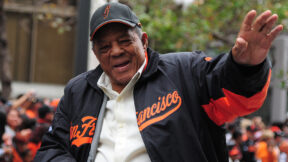 Willie Mays smiling while wearing a Giants jacket and cap